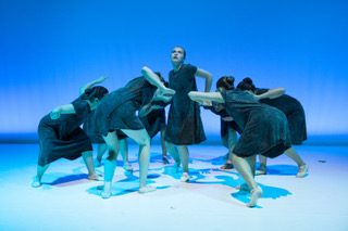 Eng zusammenstehende Tanzgruppe in dunkelgrünen Kleidern vor blauem Bühnenlicht