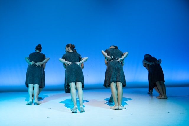 Vier Tänzerinnen von hinten mit verschränkten Armen vor blauem Bühnenlicht