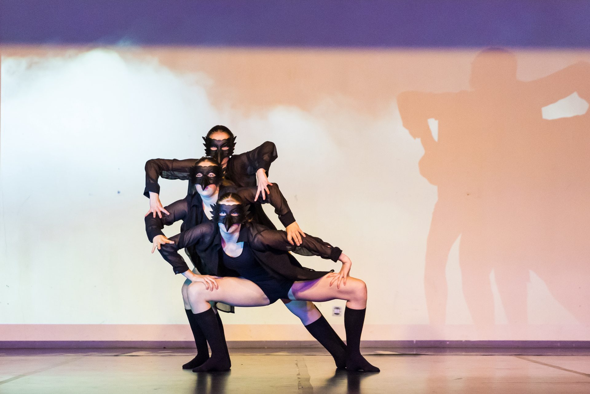 Trio in schwarzen Kostümen mit Masken in einer dramatischen Pose auf der Bühne