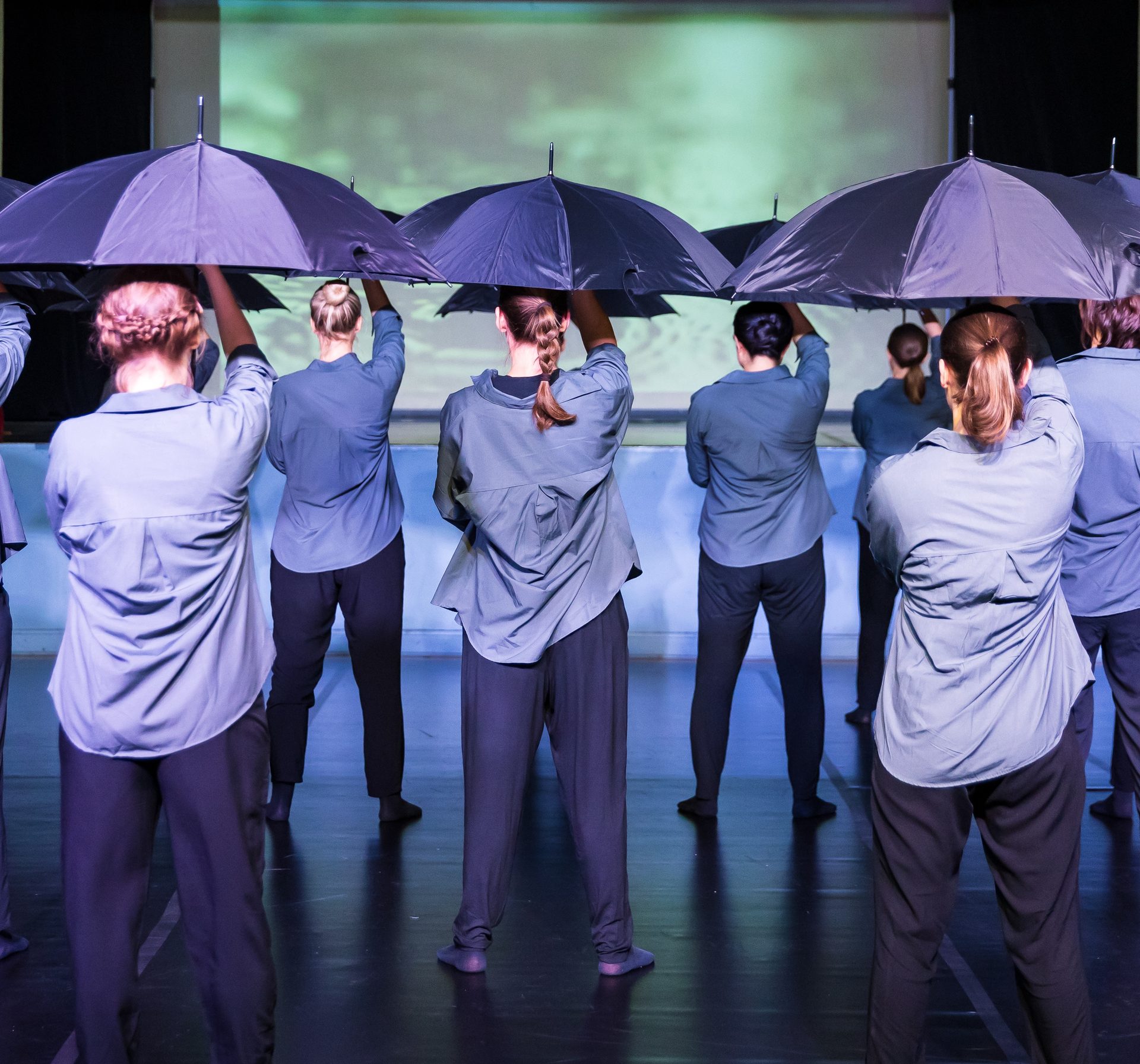 Tanzgruppe mit aufgespannten Regenschirmen von hinten gesehen auf der Bühne