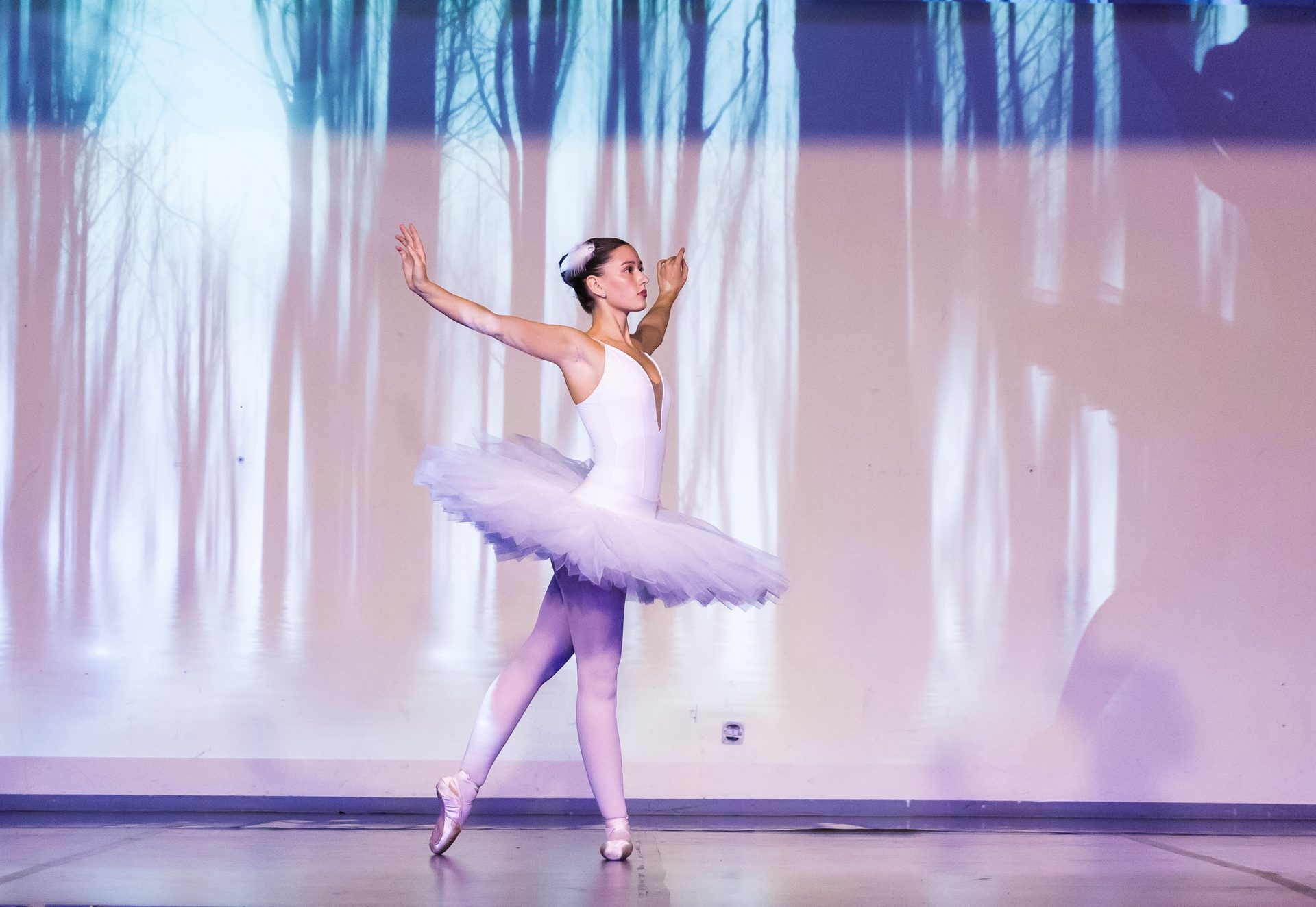Ballerina im weißen Tutu auf Spitzenschuhen vor winterlicher Waldprojektion